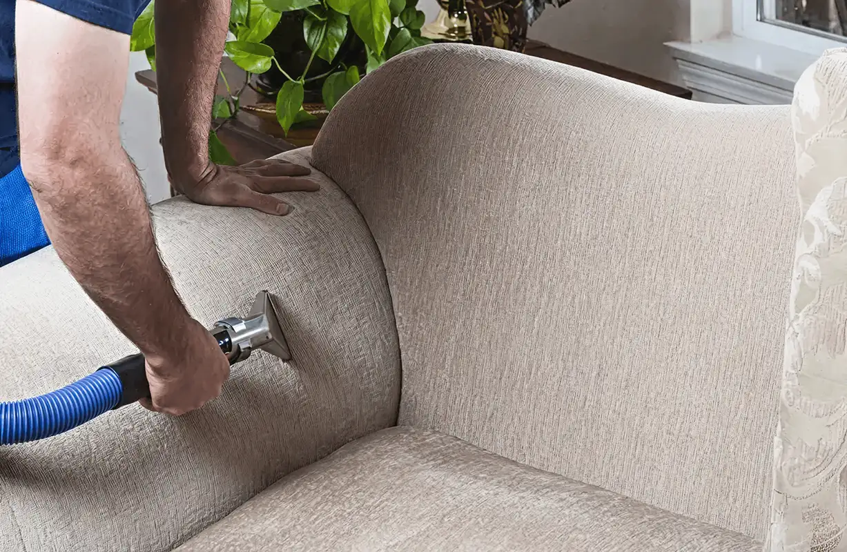 Professional upholstery cleaner deep-cleaning a fabric sofa with a handheld extraction tool and hose, St Paul, MN.